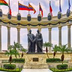 Monument to the Independence Heroes in Guayaquil, Ecuador, featuring statues of Simón Bolívar and José de San Martín surrounded by flags of Latin American countries and classical columns under a bright sky.