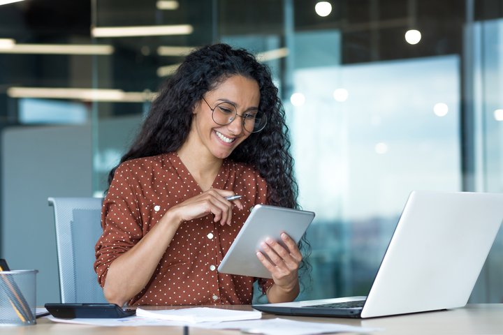 Smiling office worker using tablet and laptop for returns administration.