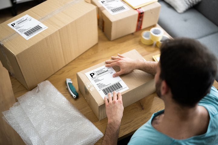 Man preparing e-commerce parcels by applying shipping labels to cardboard boxes